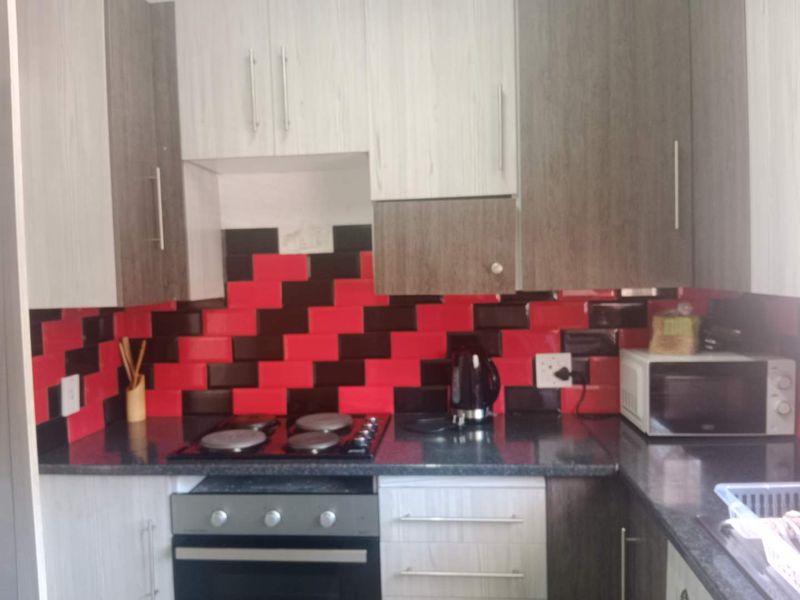 Compact kitchen featuring two-tone cabinetry, dark laminate countertops, and a bold red and black tiled backsplash with integrated oven and hob.