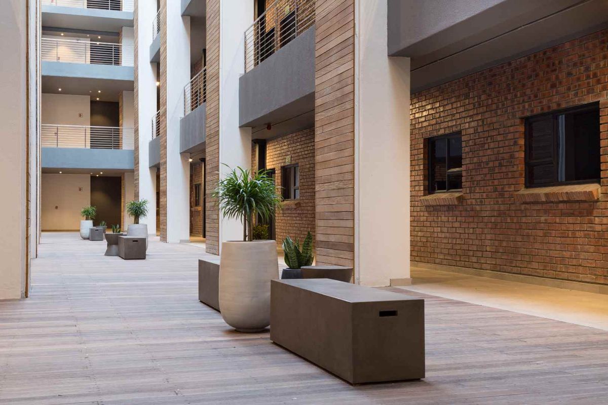 A modern apartment complex courtyard featuring exposed brick walls, timber cladding, and clean timber decking with metal balustrades on the upper levels.
