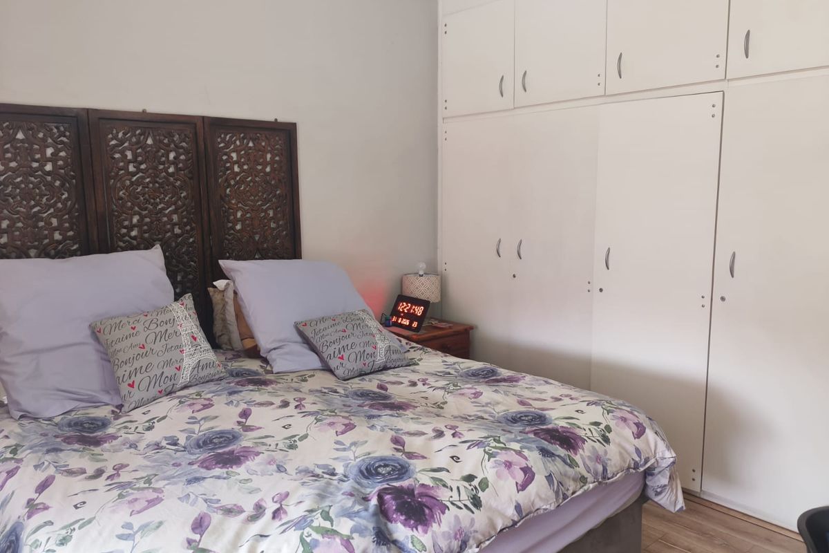 A bedroom featuring built-in white cupboards and laminate flooring, providing functional storage space.