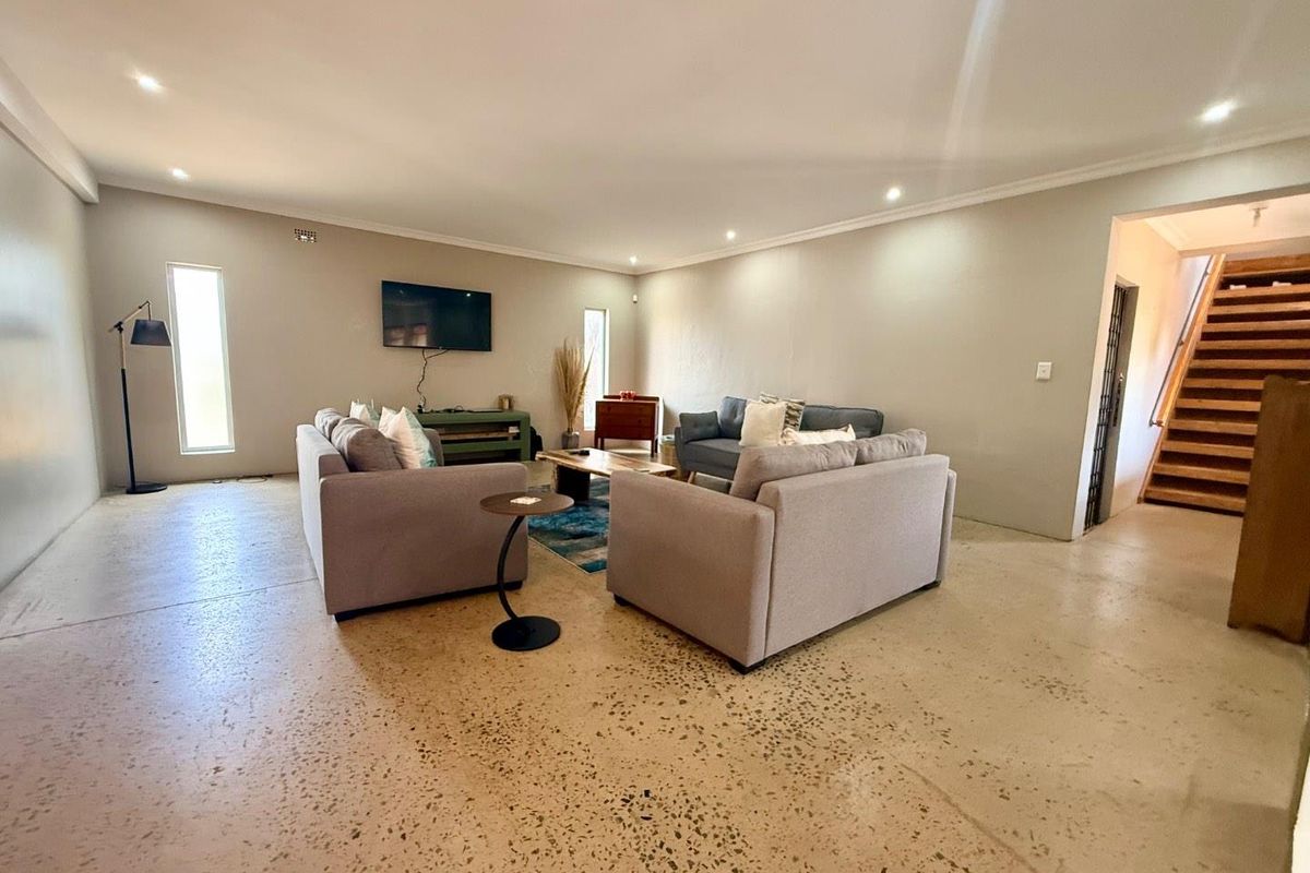 Spacious living area featuring polished concrete flooring, recessed downlighting, and an open-plan layout with an adjacent staircase.