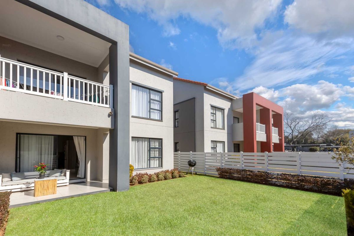 A well-maintained apartment exterior featuring a private garden, a covered patio area, and modern building architecture with white fencing.