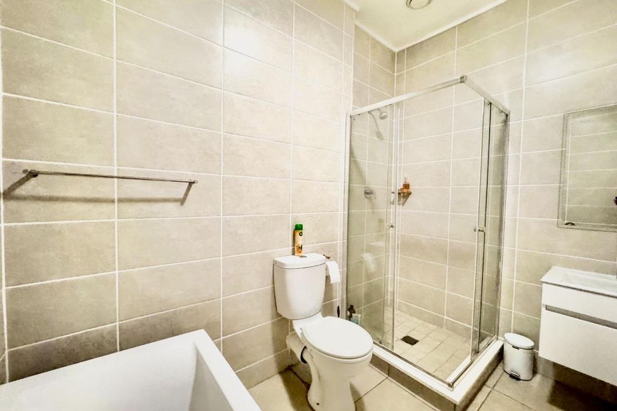 Modern bathroom featuring a glass-enclosed shower, a white vanity unit, and a toilet, finished with neutral wall and floor tiling.