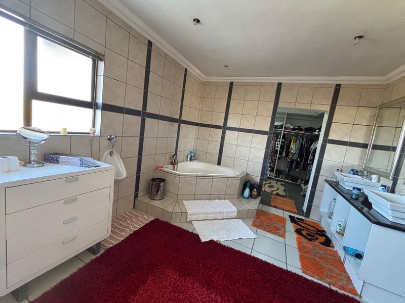 Spacious bathroom featuring a corner bathtub, double vanity, and a wall-mounted urinal, with direct access to a walk-in closet.
