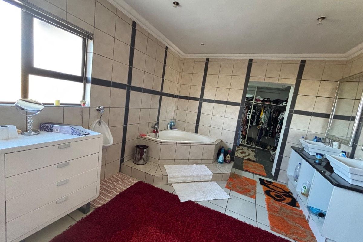 Spacious bathroom featuring a corner bathtub, double vanity, and a wall-mounted urinal, with direct access to a walk-in closet.