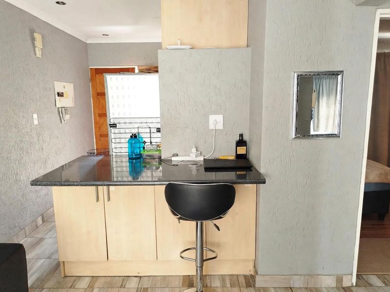 A compact kitchen area featuring a granite breakfast bar, light wood cabinetry, and textured grey walls, providing a functional space for casual dining.