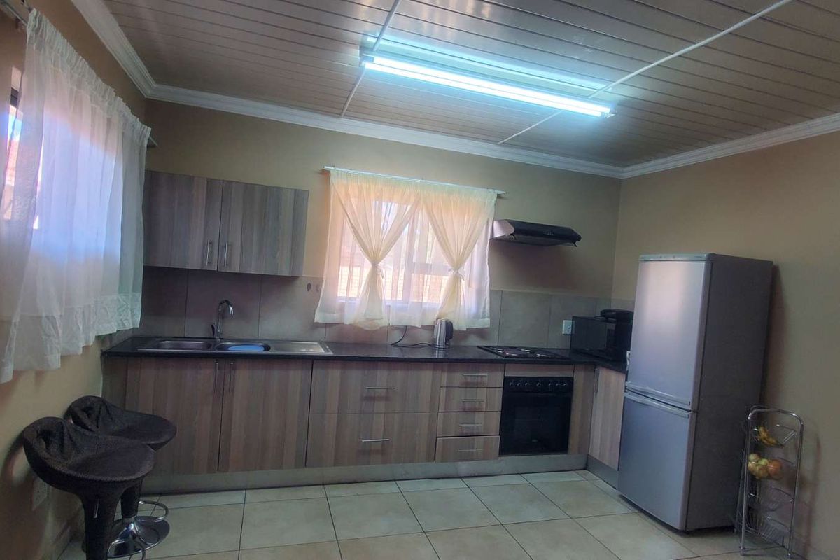 A functional kitchen featuring wood-look cabinetry, a built-in oven, hob, extractor fan, and tiled flooring with a clean, straightforward layout.