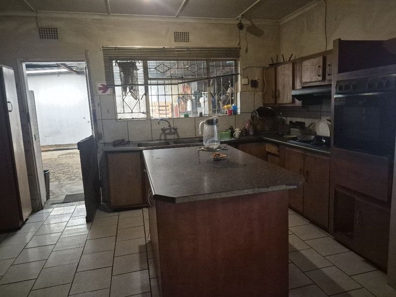 A dated kitchen featuring a central island, built-in oven, extractor fan, and tiled flooring, with direct access to an outdoor area.