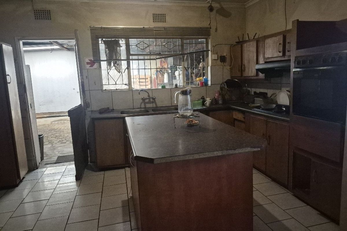 A dated kitchen featuring a central island, built-in oven, extractor fan, and tiled flooring, with direct access to an outdoor area.