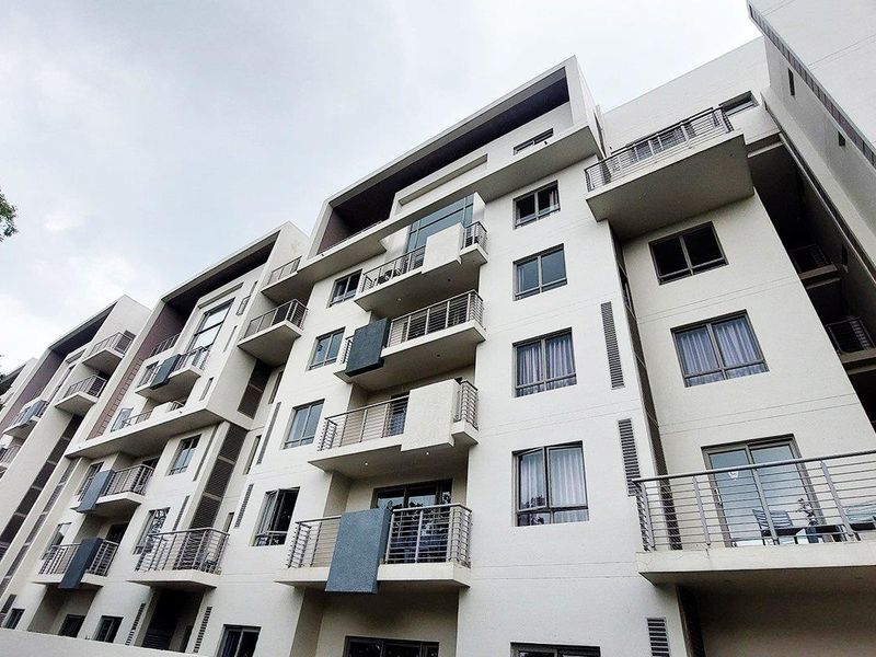 A low-angle view of a modern multi-story apartment building featuring concrete facade, multiple balconies with metal railings, and large glass windows.