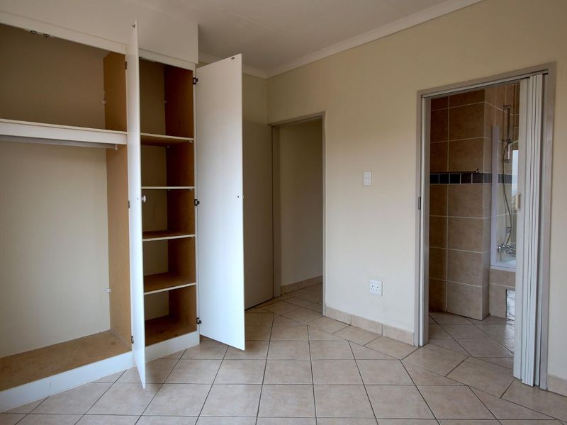 An empty bedroom featuring tiled flooring, a built-in wardrobe, and direct access to an en-suite bathroom with a folding door.