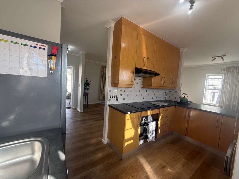 Functional kitchen featuring timber veneer cabinetry, laminate countertops, built-in oven, electric cooktop, and decorative tile splashback, with adjacent open-plan living area.