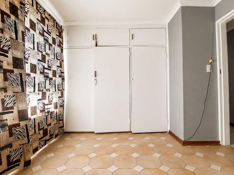 A bedroom featuring built-in cupboards and tiled flooring, offering a clean, neutral space ready for personalization.
