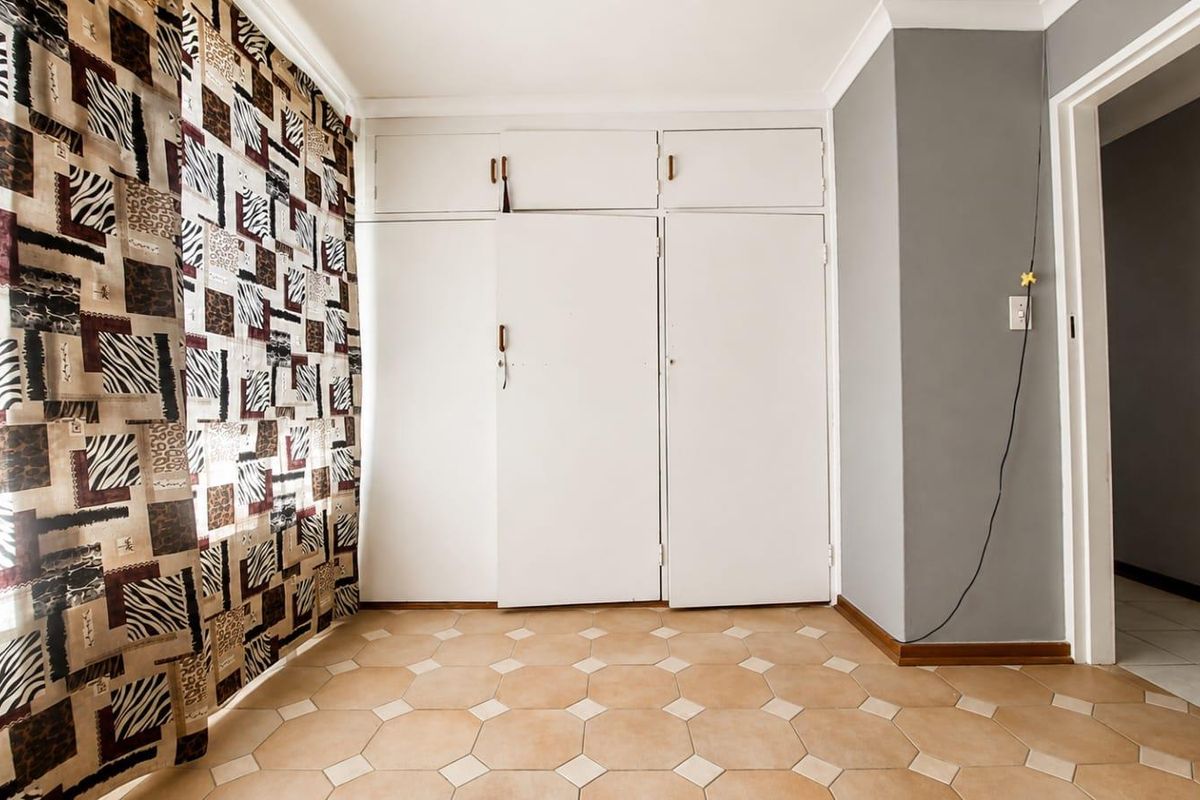A bedroom featuring built-in cupboards and tiled flooring, offering a clean, neutral space ready for personalization.