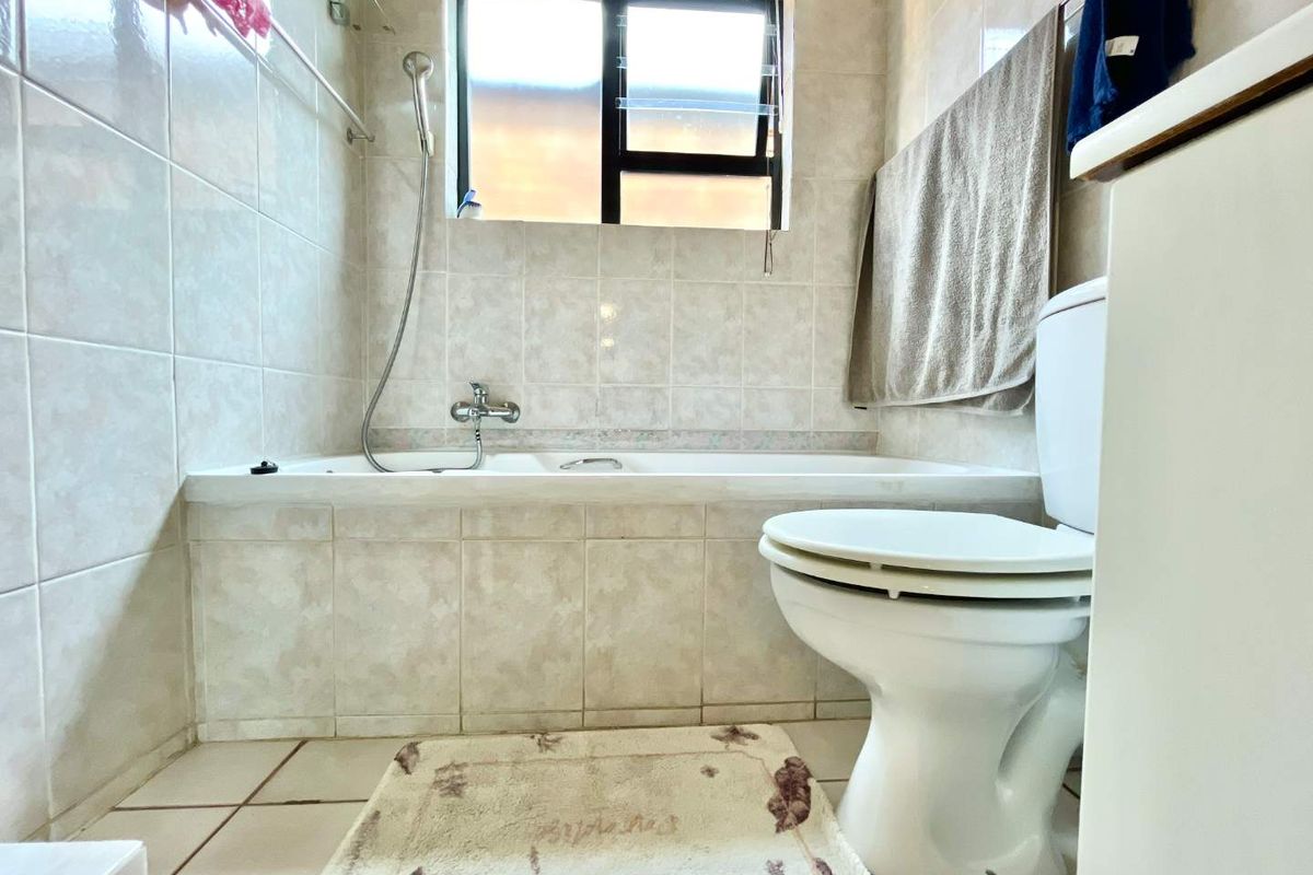 A functional bathroom featuring a built-in bathtub with shower mixer, toilet, and neutral wall and floor tiling.