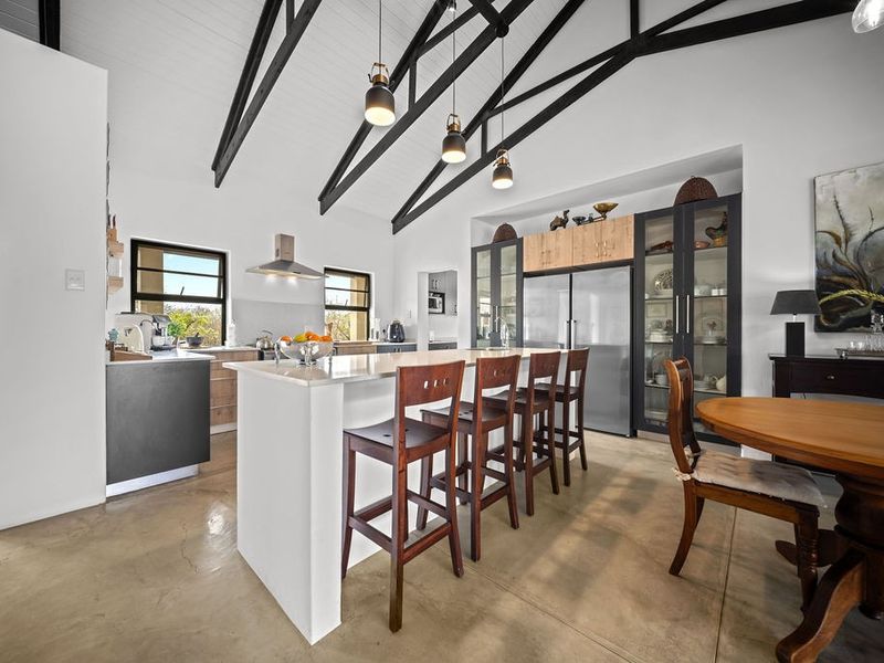 Spacious open-plan kitchen and dining area featuring high vaulted ceilings with exposed trusses, polished concrete floors, and a modern central island.