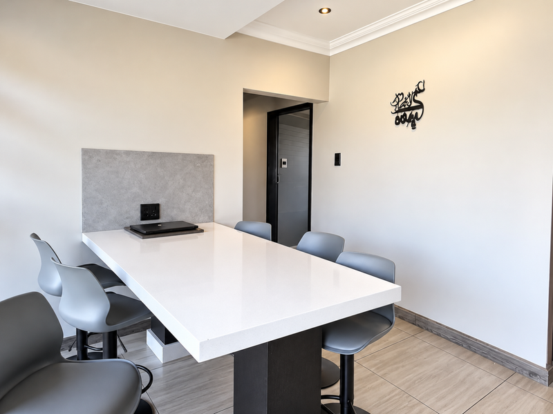 A modern dining area featuring a sleek built-in breakfast bar with a stone countertop, complemented by neutral walls and contemporary tiled flooring.