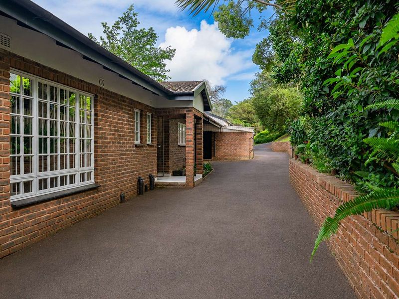 A well-maintained townhouse exterior featuring a face brick facade, a paved driveway, and a covered entrance porch surrounded by established greenery.