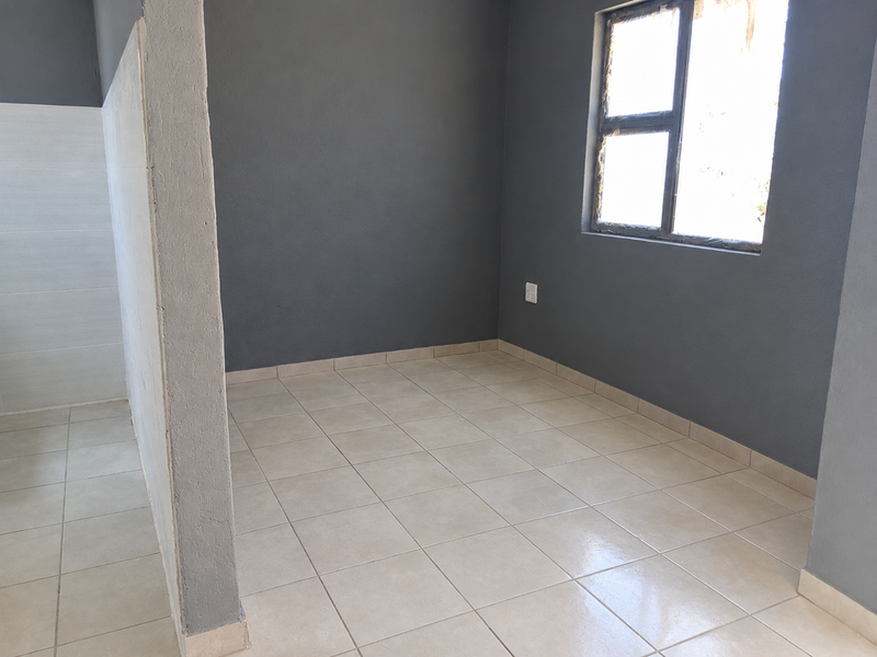 An empty bedroom featuring neutral tiled flooring, dark grey painted walls, and an aluminium window frame, offering a blank canvas for interior design.