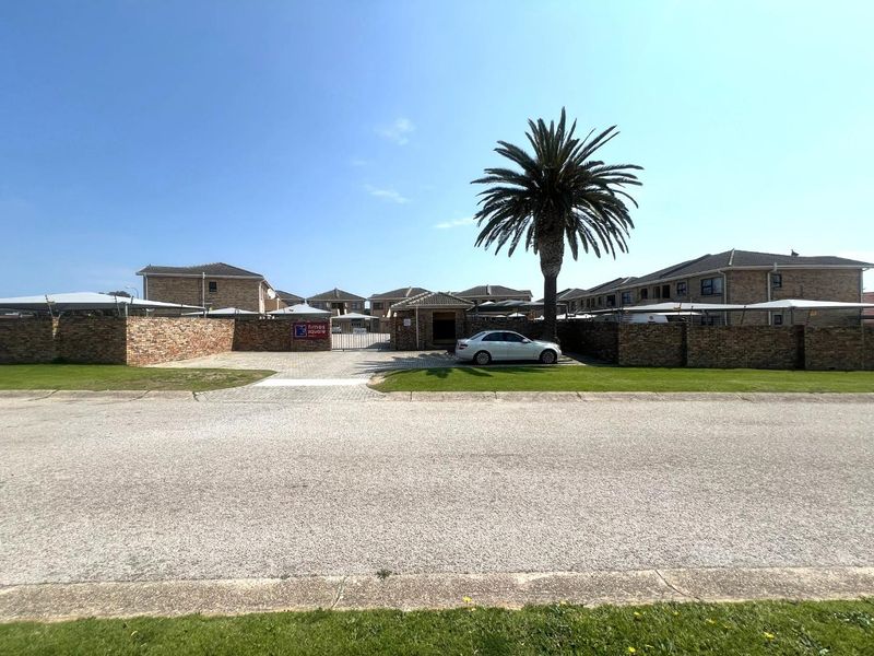 Street view of the apartment complex entrance featuring a brick boundary wall, paved driveway, and secure gated access.