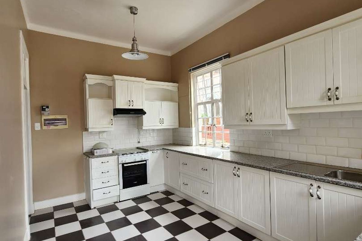 A bright, empty kitchen featuring white cabinetry, granite countertops, subway tile backsplash, and classic checkerboard floor tiles.