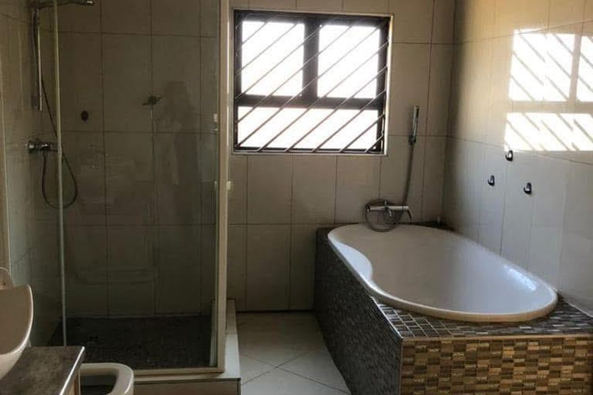 A functional bathroom featuring a built-in bathtub, separate shower enclosure, vanity cabinet, and tiled finishes throughout.