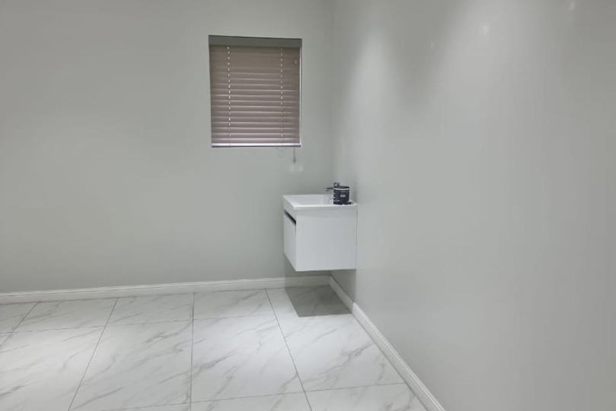 A clean, modern interior space featuring white marble-look floor tiles, recessed ceiling lighting, and a wall-mounted vanity basin.