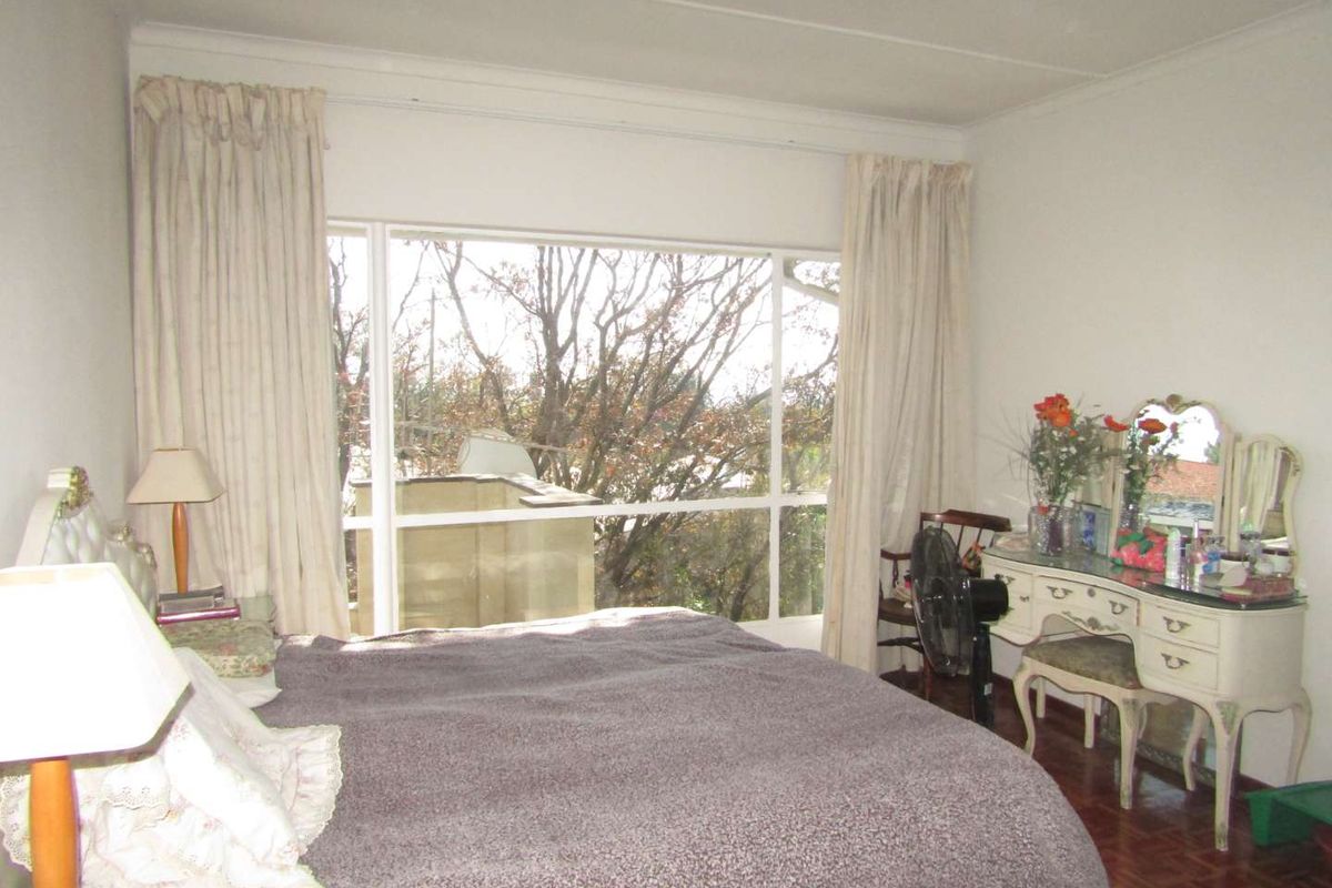 A bedroom featuring large windows that provide natural light and views, with parquet flooring and neutral wall finishes.