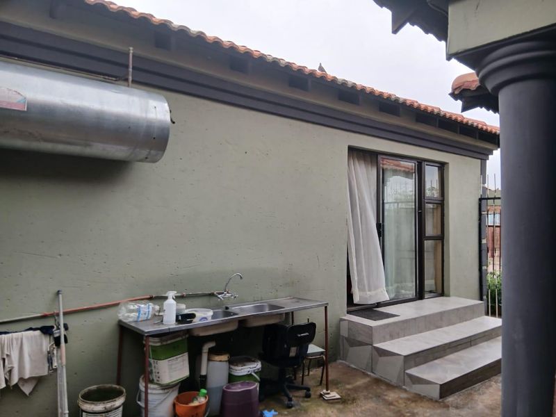 Rear exterior view featuring a tiled step entrance, sliding glass door, and an external stainless steel sink unit with exposed plumbing.