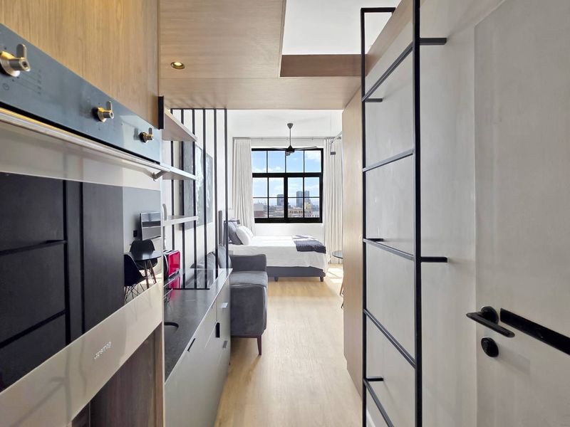 Modern open-plan studio apartment featuring a sleek kitchen with built-in appliances, light wood flooring, and a mezzanine ladder leading to a bright sleeping area.