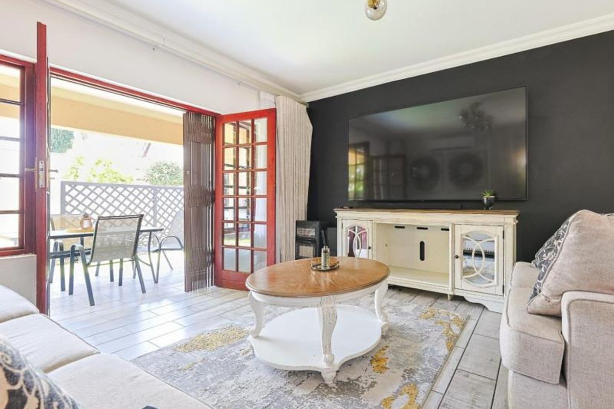 A bright living room featuring tiled flooring, crown molding, and large french doors providing direct access to an outdoor patio area.