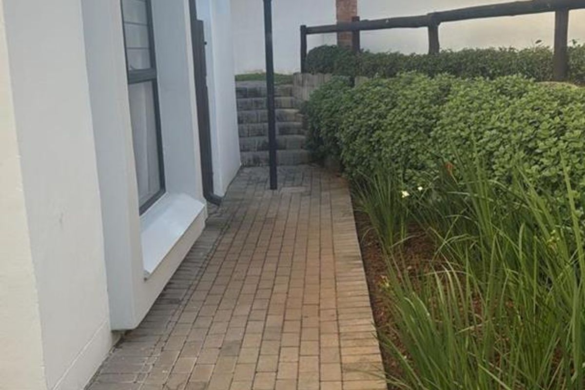A paved side walkway leading to a garden area, featuring a perimeter wall with electric fencing and integrated garden lighting.