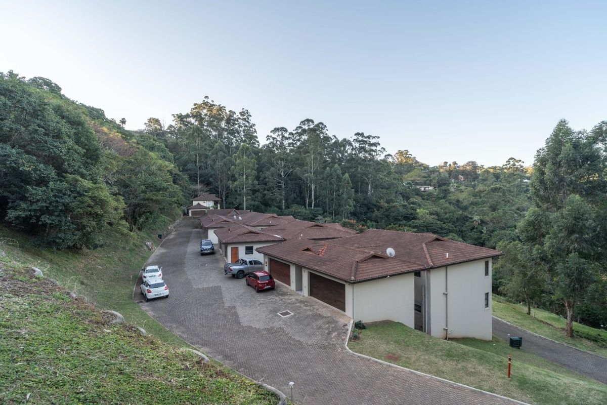 Aerial view of a townhouse complex featuring tiled roofs, paved driveways, and integrated garages, set against a lush, forested hillside.