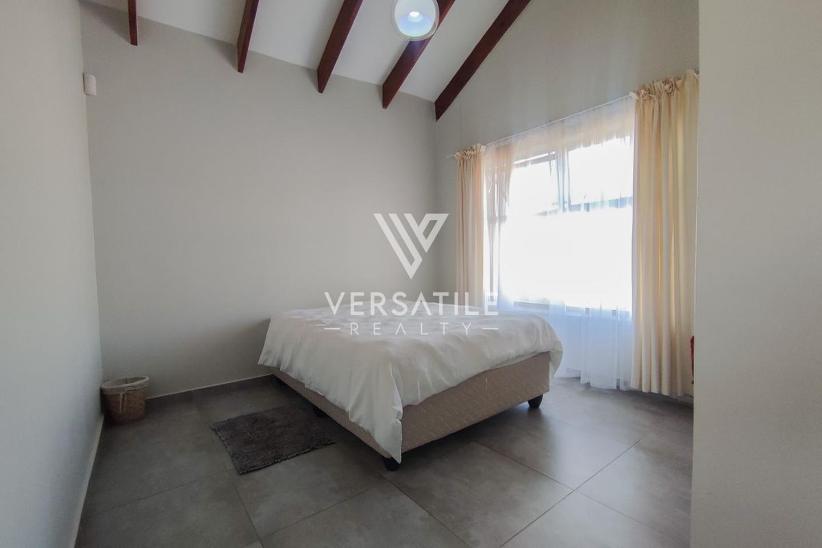 Spacious bedroom featuring high vaulted ceilings with exposed timber beams and large tiled flooring.