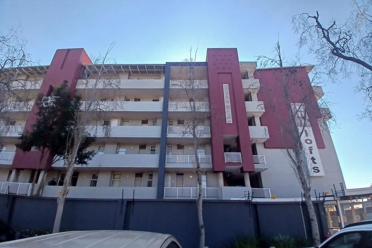 Front elevation of a multi-story apartment complex featuring balconies with metal railings and secure perimeter fencing.
