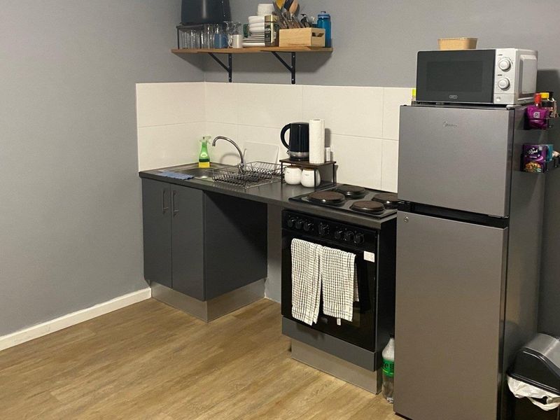 A compact kitchen area featuring a sink, electric stove, oven, tiled splashback, and base cabinetry with wood-look flooring.
