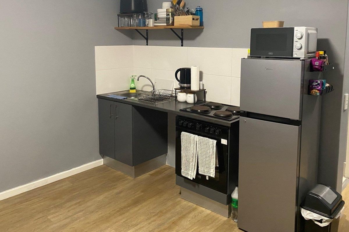 A compact kitchen area featuring a sink, electric stove, oven, tiled splashback, and base cabinetry with wood-look flooring.