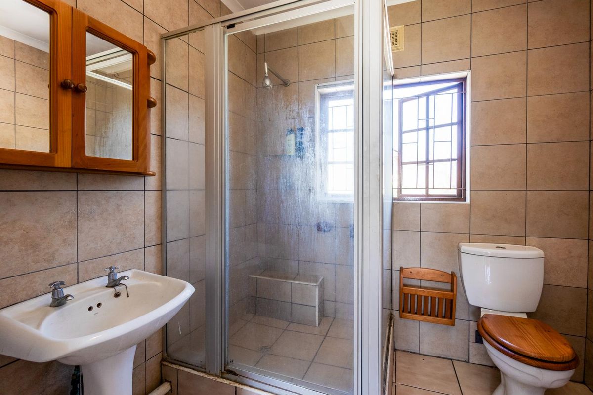 A functional bathroom featuring a tiled shower enclosure, pedestal basin, and toilet, finished with neutral wall and floor tiles.