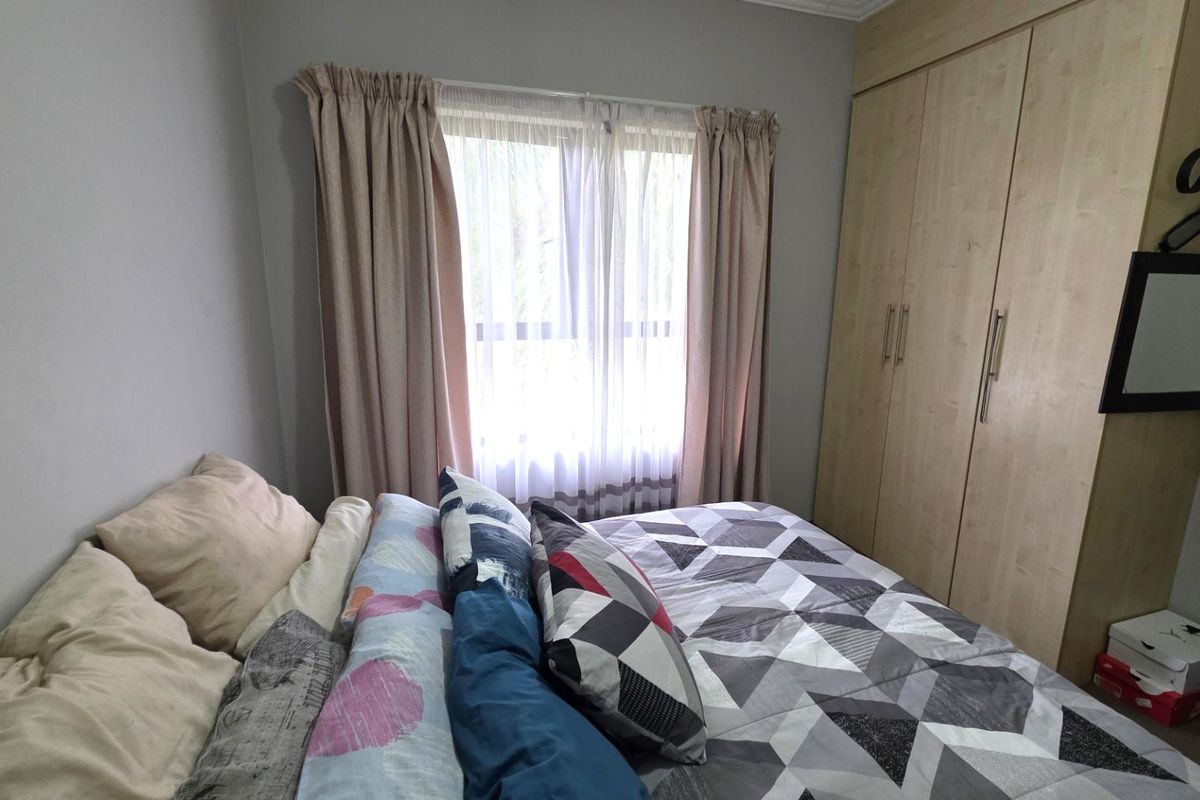 A bedroom featuring light wood-finish built-in wardrobes and a window with curtains.