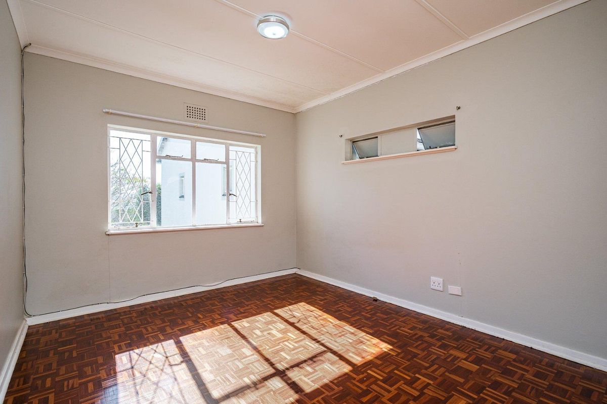 An empty bedroom featuring classic parquet flooring, security bars on the windows, and neutral wall finishes, offering a blank canvas for personalization.