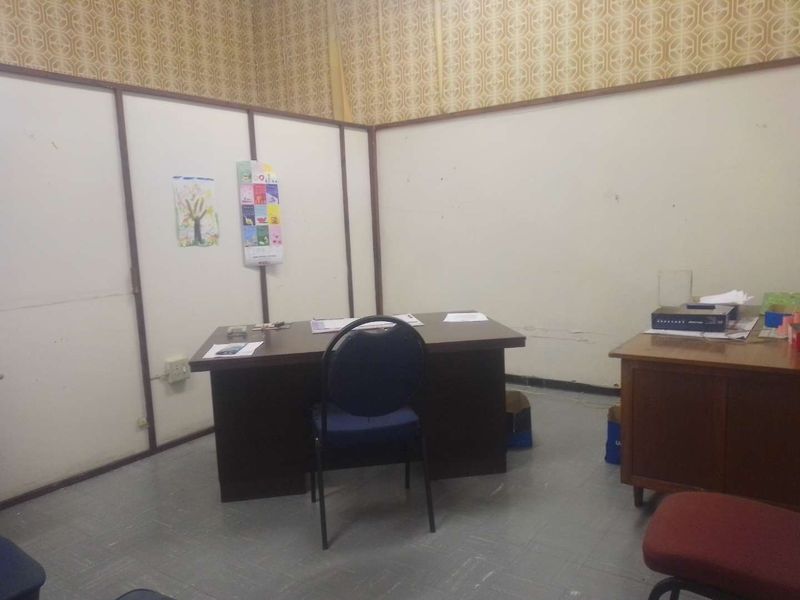 A functional office space featuring partition walls, vinyl flooring, and dated wallpaper, suitable for renovation or modernization.