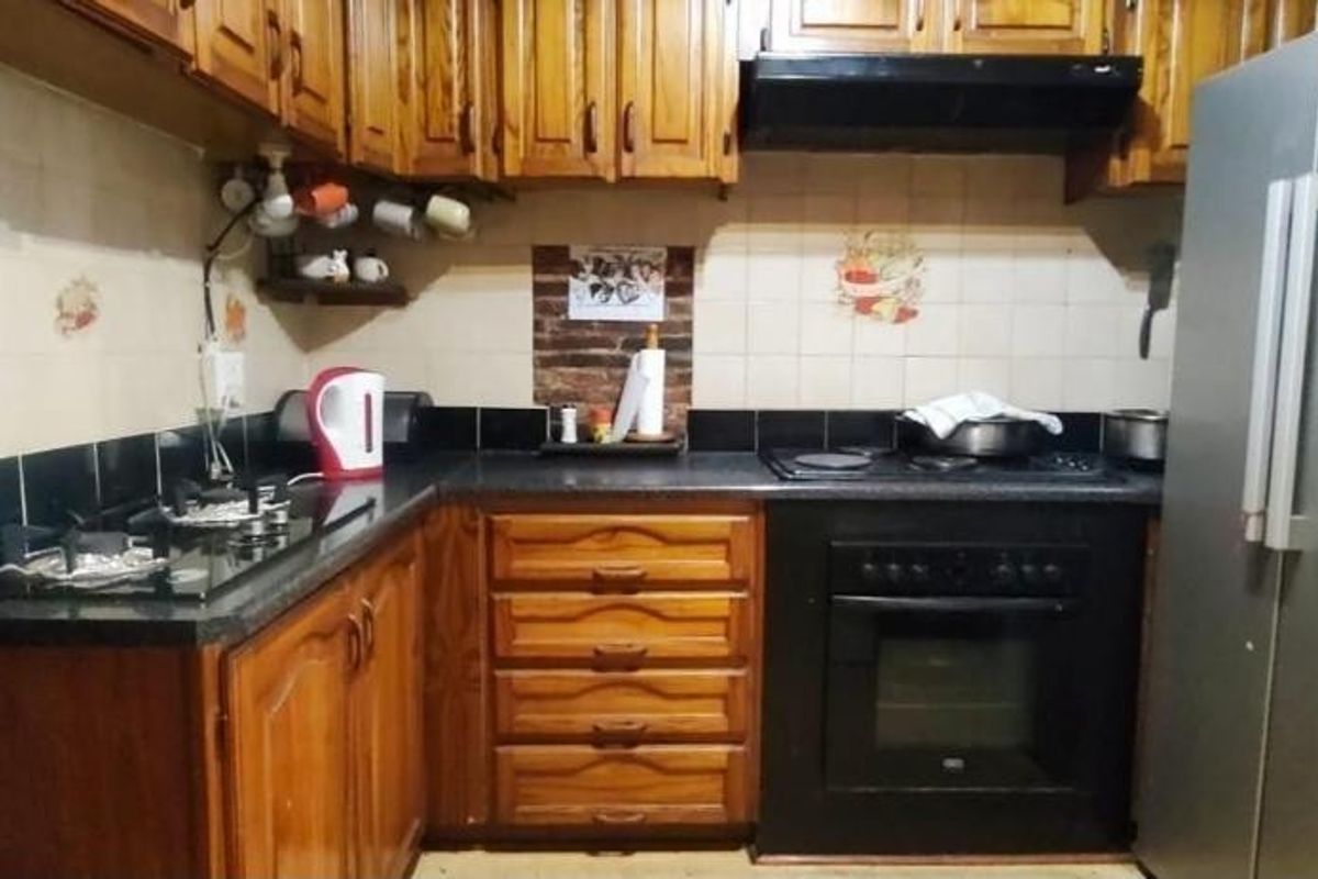 A functional kitchen featuring traditional wooden cabinetry, dark stone countertops, a built-in oven, and a gas hob with an integrated extractor fan.