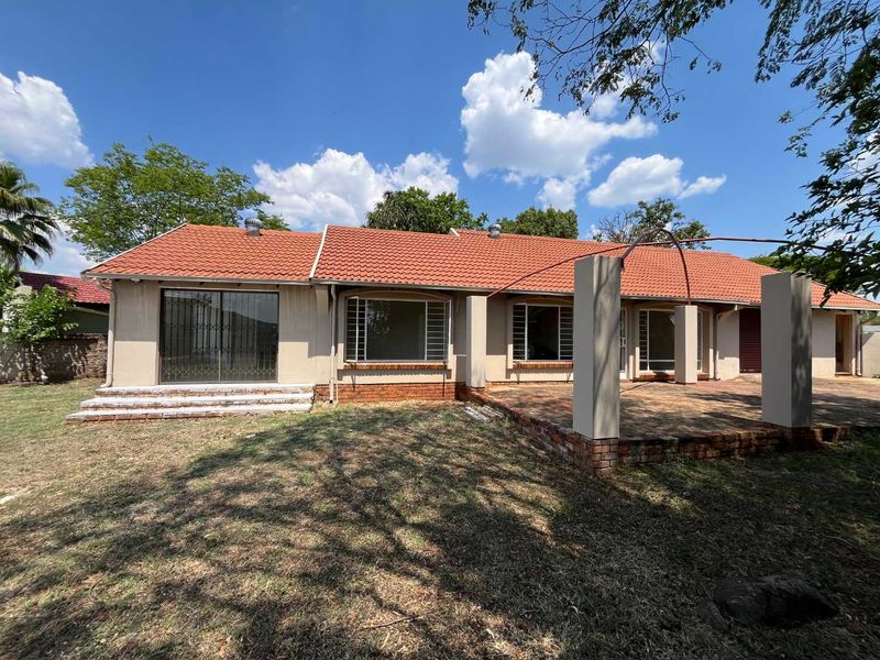 Rear view of the house featuring a terracotta tiled roof, a spacious brick patio with concrete pillars, and sliding glass doors with security gates.