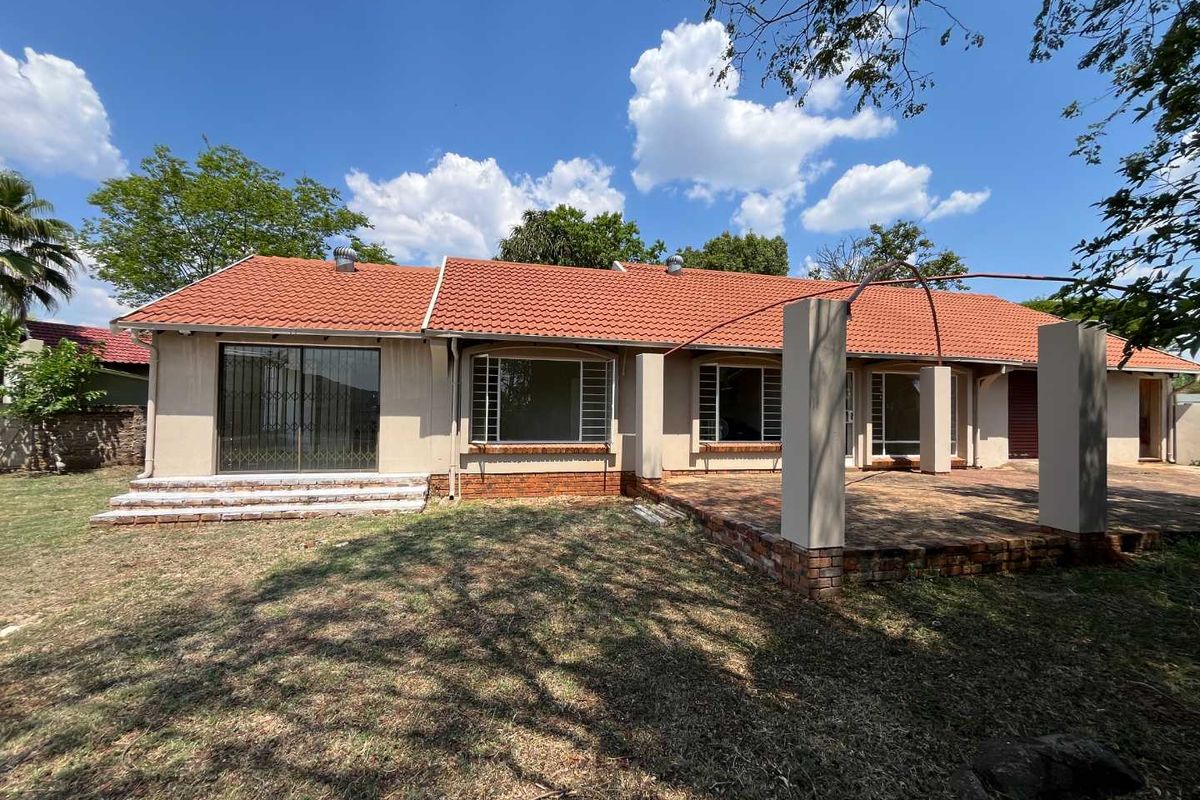 Rear view of the house featuring a terracotta tiled roof, a spacious brick patio with concrete pillars, and sliding glass doors with security gates.