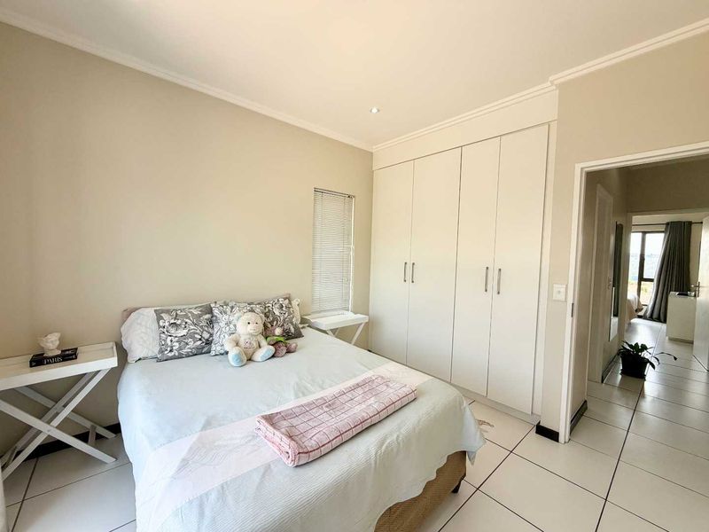 A well-maintained bedroom featuring neutral walls, tiled flooring, built-in cupboards, and natural light through a window with venetian blinds.