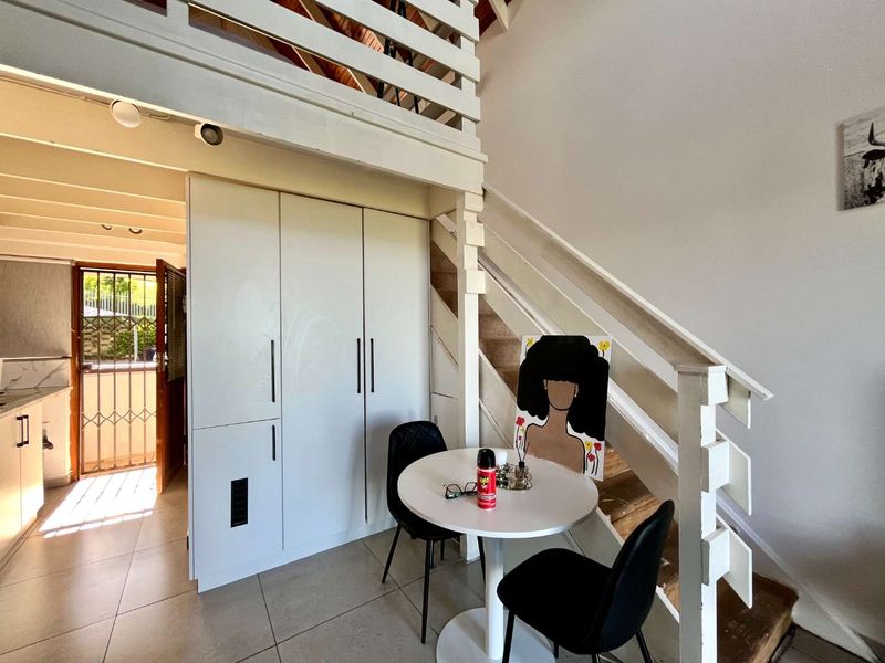 Open plan living area featuring a staircase leading to a mezzanine level, built-in storage cabinetry, and tiled flooring with access to an exterior entrance.