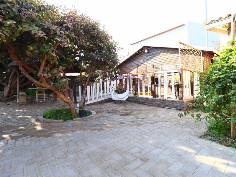 A rear garden area featuring a paved patio, a timber-clad structure with a deck, and a mature tree providing shade.