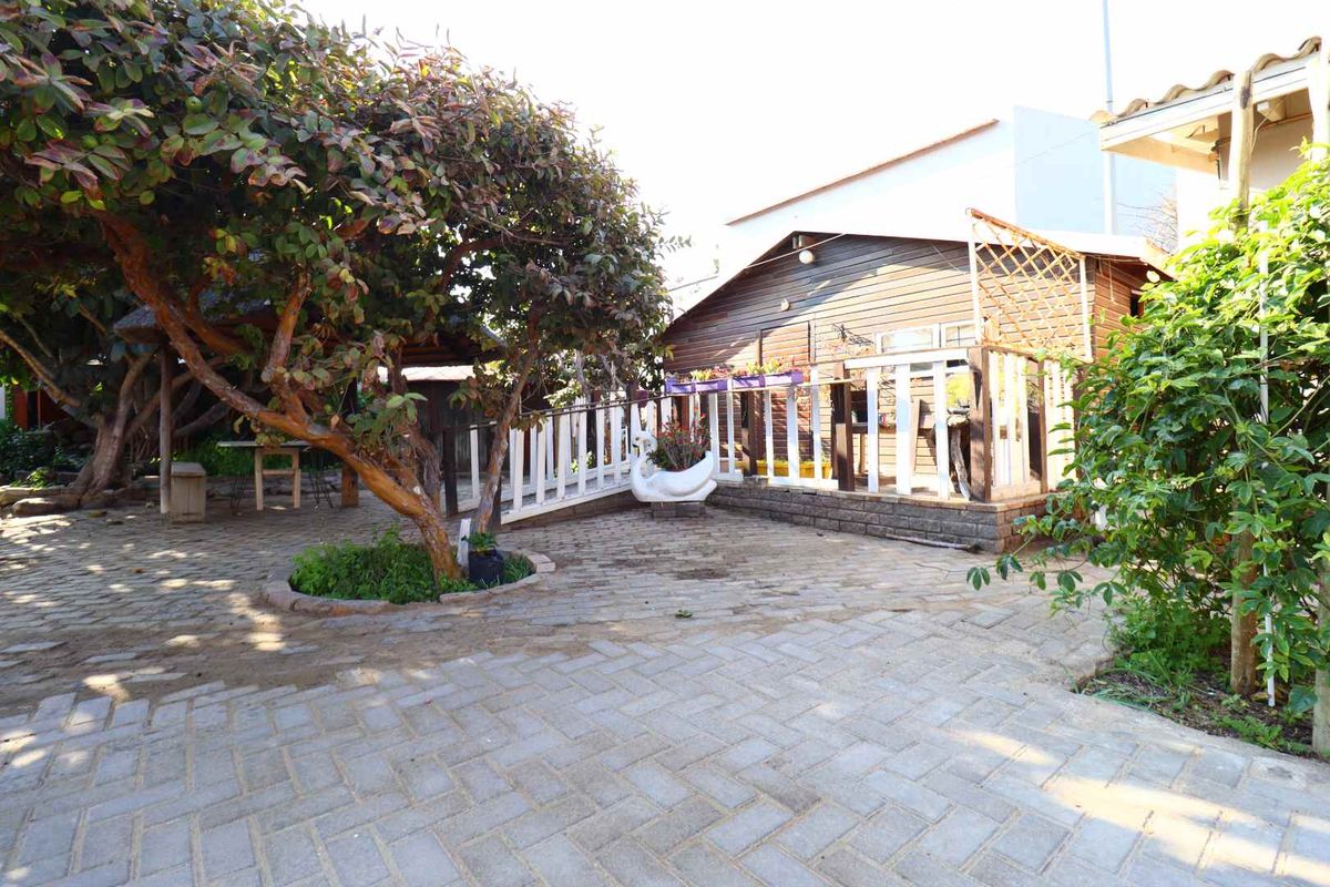 A rear garden area featuring a paved patio, a timber-clad structure with a deck, and a mature tree providing shade.
