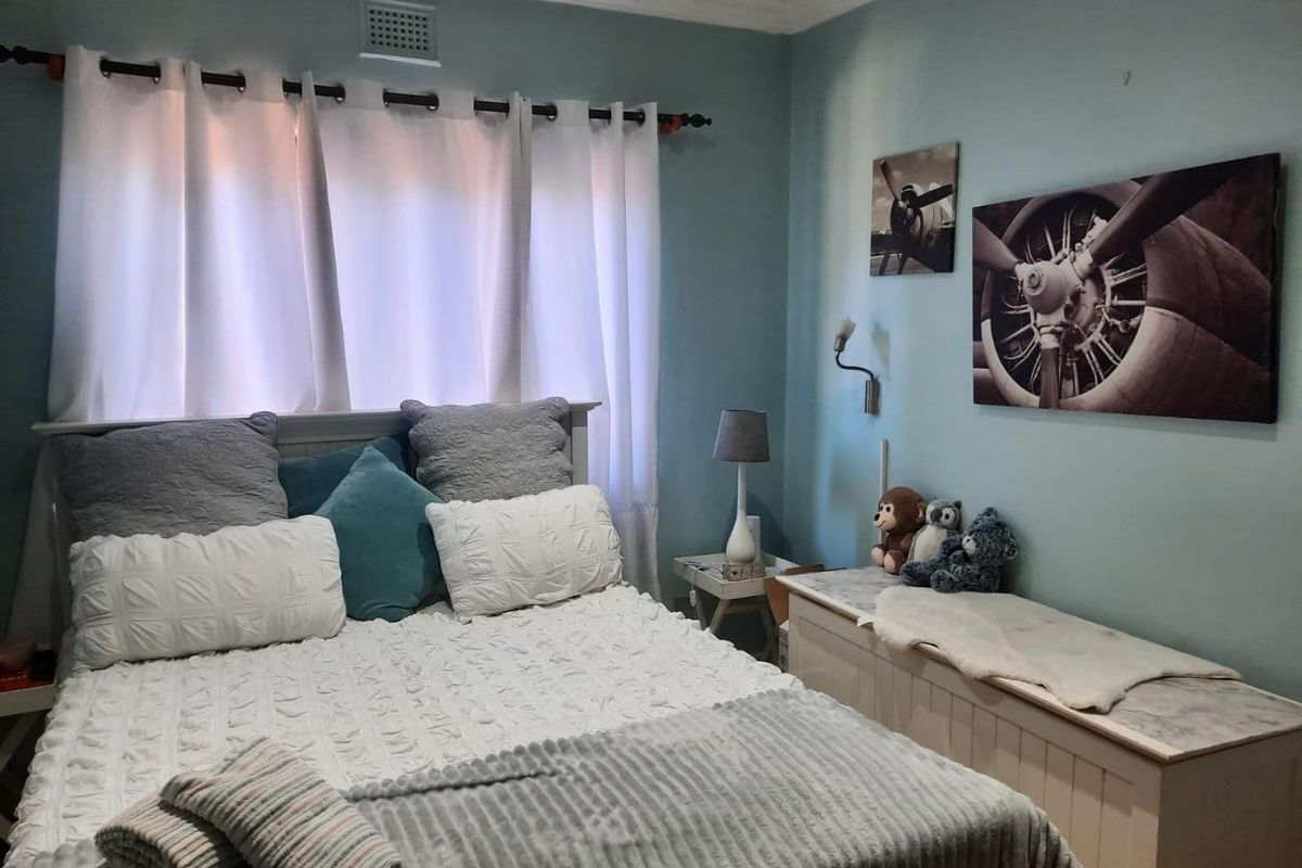 A cozy bedroom featuring light blue walls, decorative ceiling cornicing, and a wall-mounted light fixture.
