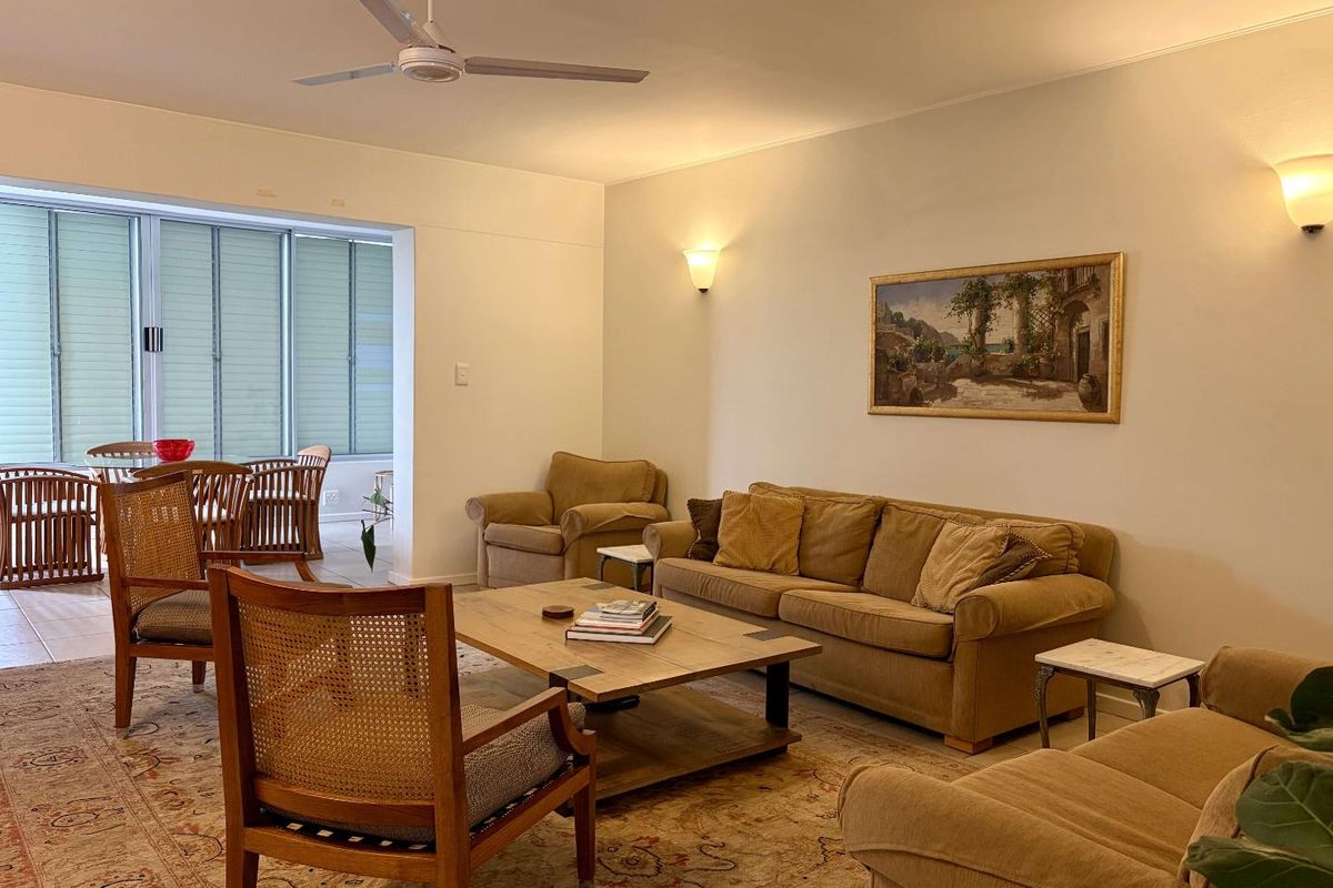 Spacious living room featuring a ceiling fan, wall sconce lighting, and large sliding glass doors leading to an adjacent sunroom or balcony area.