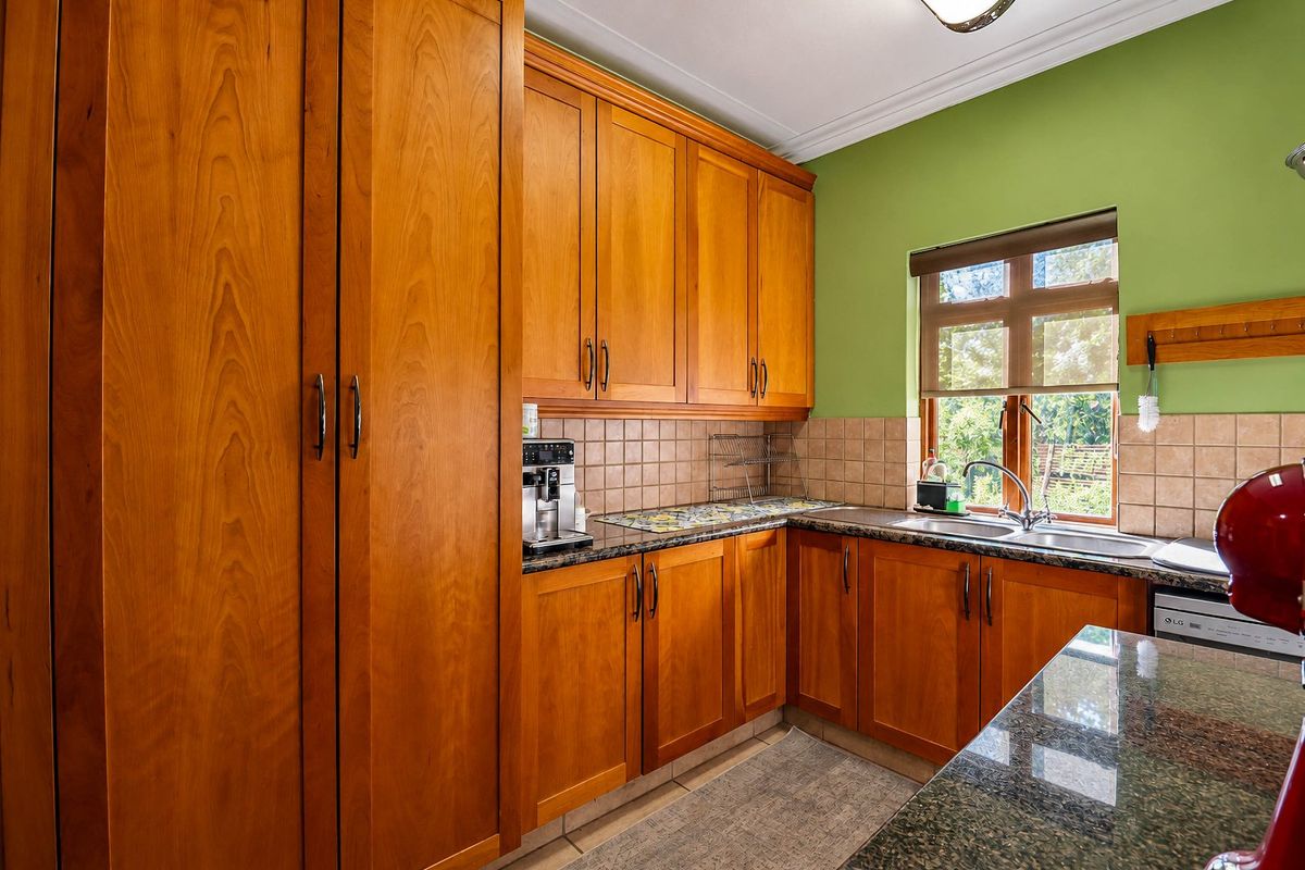 A functional kitchen featuring warm wooden cabinetry, granite countertops, a double basin sink, and a tiled backsplash with natural light from the window.